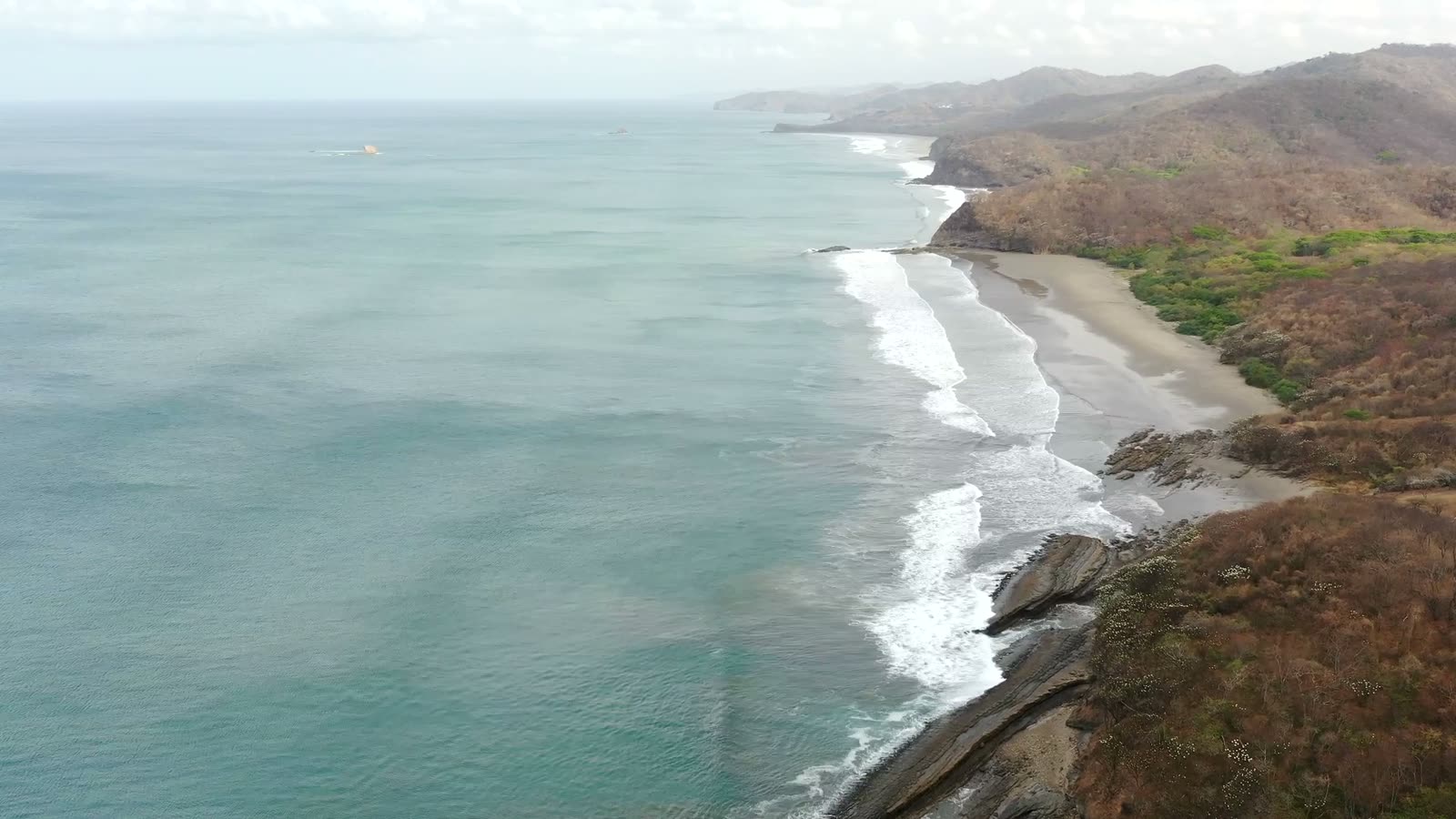 Drone view from above the rock shelf at the south end of Playa Yankee, looking north along the beach as sets wrap off the rocks
