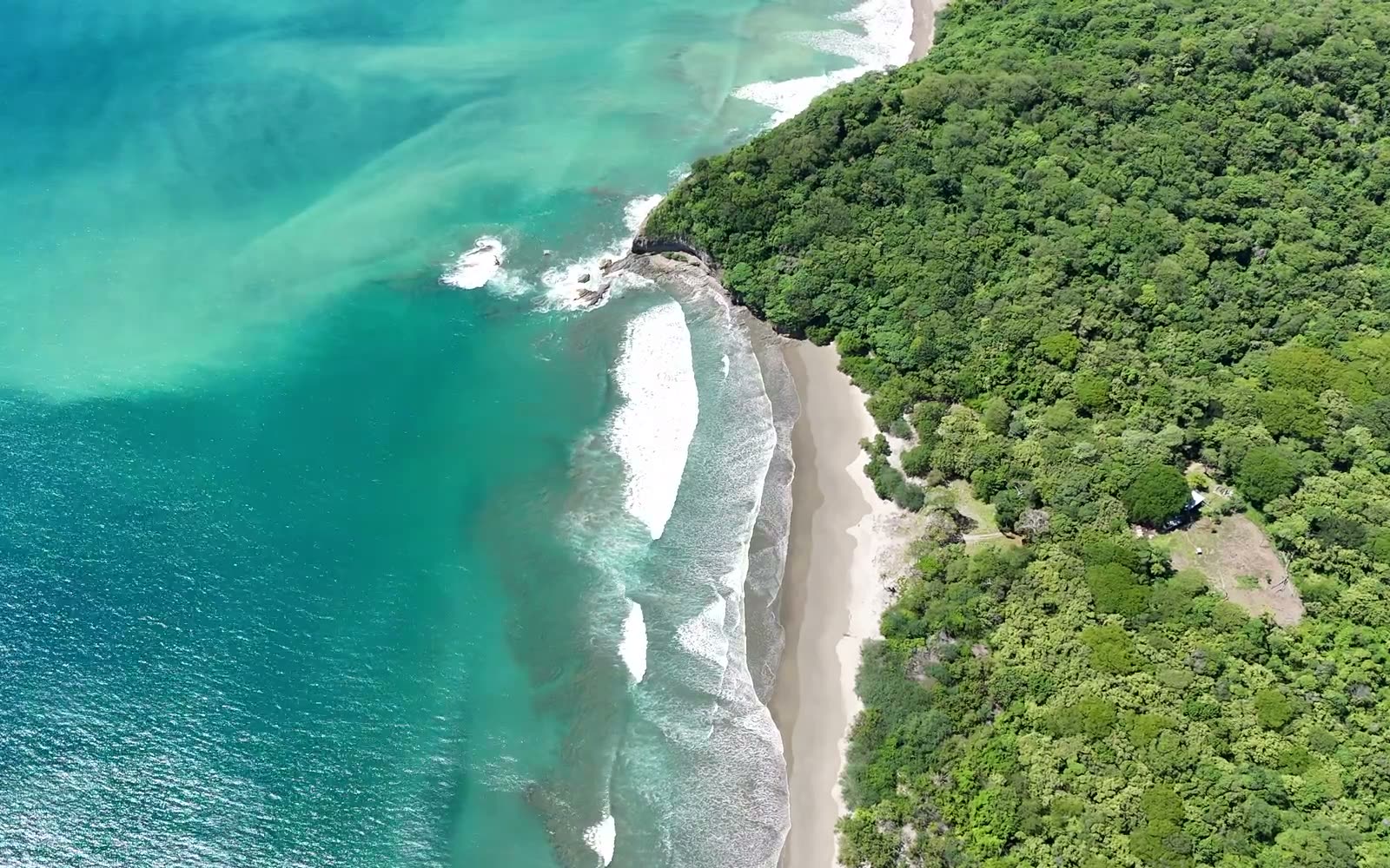 Overhead drone view of the north end of Playa Yankee: the rocky point, whitewater wrapping it, and the beach running south